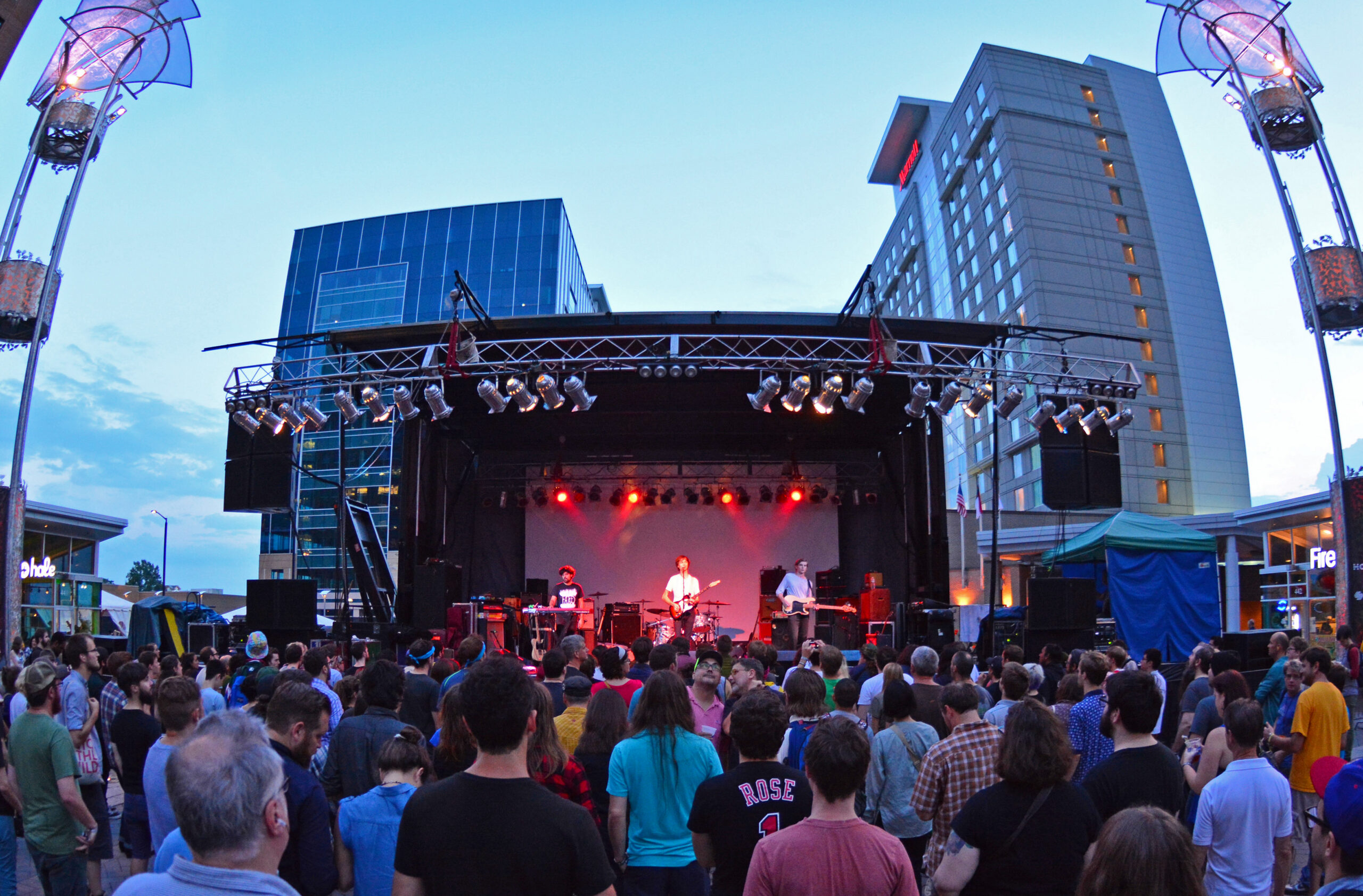 Live concert performance at Red Hat Amphitheater in downtown Raleigh, with a crowd gathered in front of the stage during an evening event.